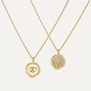 May include: Two gold necklaces with a delicate chain and a round pendant. One pendant features a textured surface and the other has a small design.
