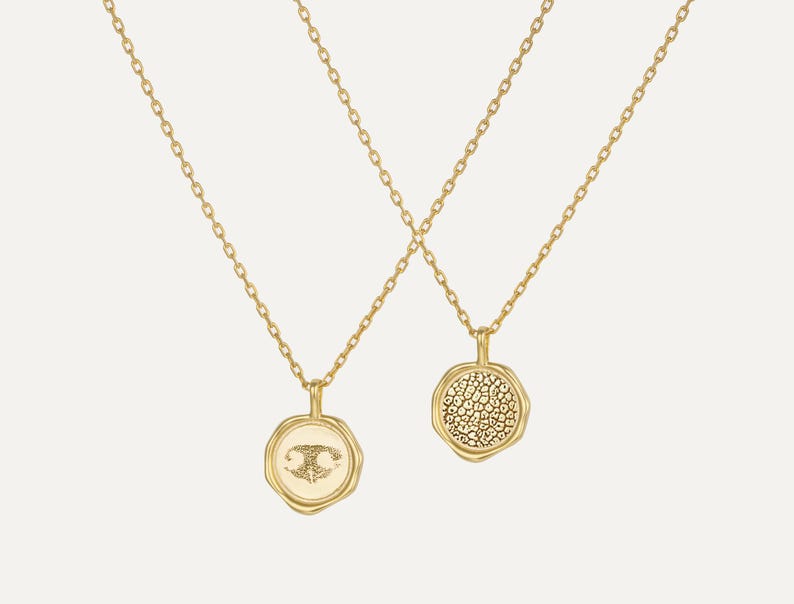 May include: Two gold necklaces with a delicate chain and a round pendant. One pendant features a textured surface and the other has a small design.