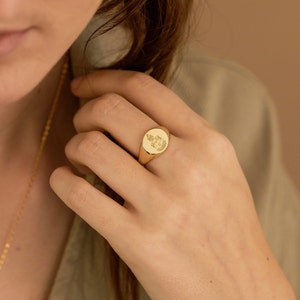 Peut inclure: Une bague signet en or avec un design de blason. La bague est de forme ovale et a une finition lisse et polie.