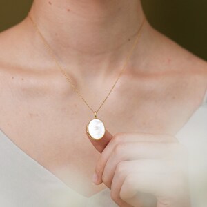 Op de afbeelding: Een gouden ketting met een witte ovale hanger.