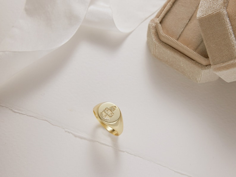 Peut inclure: Une bague signet en or avec un motif grav&eacute; d&eacute;taill&eacute;. La bague est sur une surface blanche.
