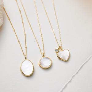 Op de afbeelding: Vier gouden kettingen met verschillende hanger stijlen. Elke hanger is gemaakt van wit parelmoer en heeft een andere vorm: ovaal, rond, hart en hart met een kleine diamant.
