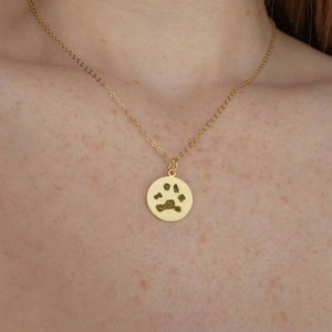 May include: A gold necklace with a round pendant featuring a paw print. The pendant is a memorial piece for a pet.
