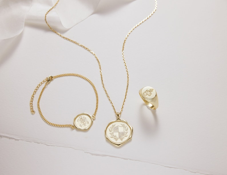 Peut inclure: Trois colliers en or avec une cha&icirc;ne d&eacute;licate et un pendentif circulaire orn&eacute; d'un motif floral. Le pendentif est grav&eacute; d'un blason.