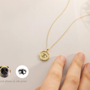 May include: Gold necklace with a round pendant featuring a black and white paw print. The pendant is on a delicate gold chain.