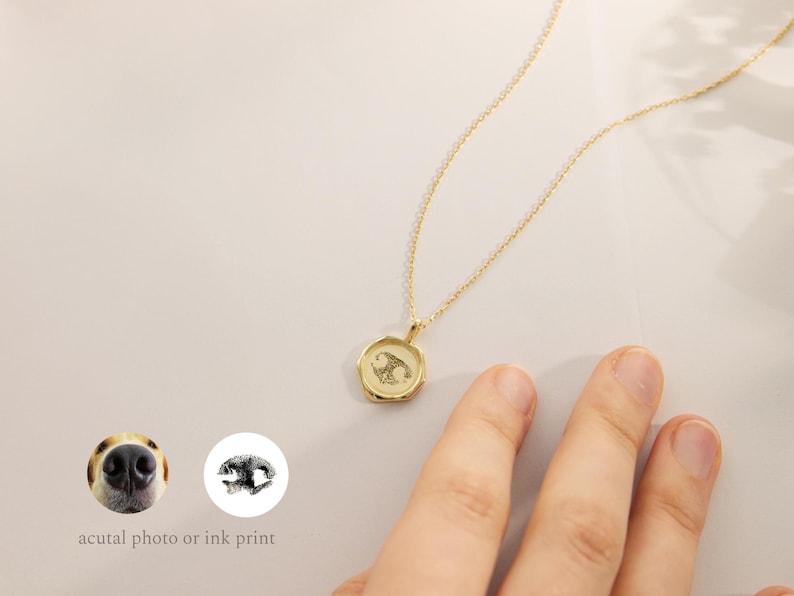 May include: Gold necklace with a round pendant featuring a black and white paw print. The pendant is on a delicate gold chain.