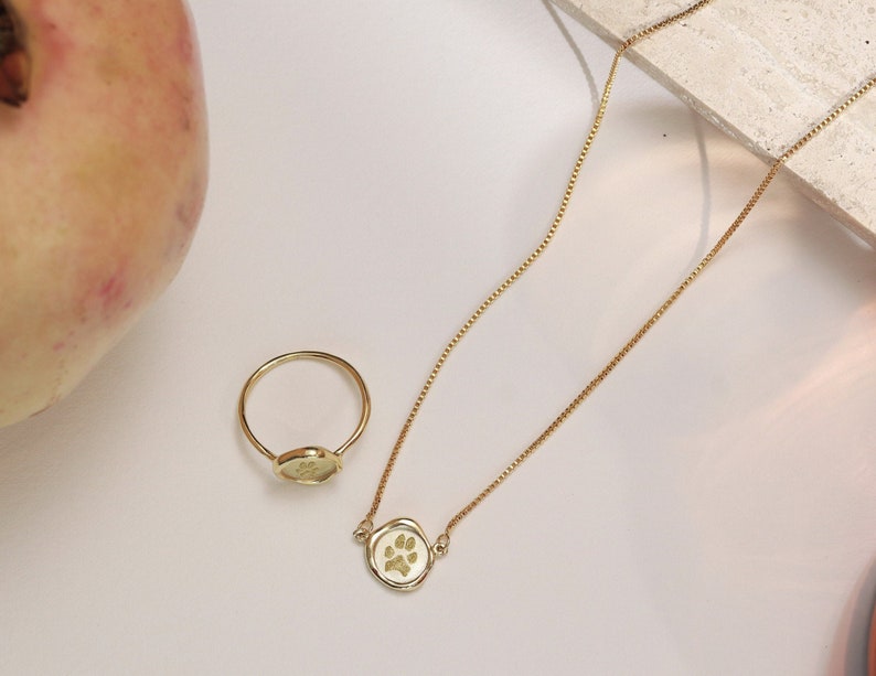 Peut inclure: Un ensemble de collier et bague en or avec un pendentif en forme de patte de chien. Le collier a une cha&icirc;ne d&eacute;licate et la bague est simple et &eacute;l&eacute;gante.