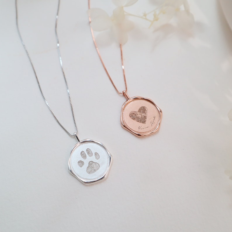 May include: Two silver necklaces with pendants. One pendant is a silver octagon with a paw print engraved inside. The other pendant is a rose gold octagon with a heart engraved inside. The rose gold pendant has the text "You are my best friend" engraved on it.