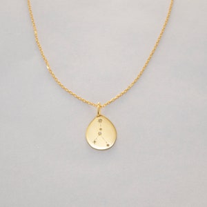 May include: Gold necklace with a teardrop-shaped pendant featuring the Cancer constellation with small diamonds.