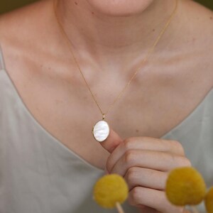 Op de afbeelding: Een gouden ketting met een witte ovale hanger.