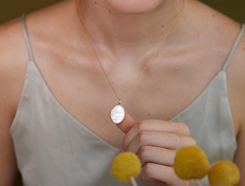 Op de afbeelding: Een gouden ketting met een witte ovale hanger.