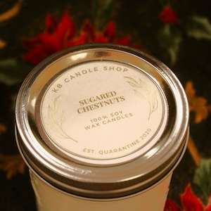 Peut inclure: Un couvercle de bocal en argent avec une étiquette blanche sur laquelle est inscrit "KB Candle Shop Sugared Chestnuts 100% Soy Wax Candles Est. Quarantine 2020".