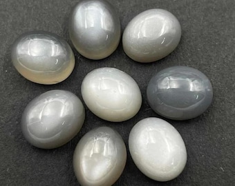 Puede incluir: Un surtido de siete piedras preciosas ovaladas pulidas en tonos grises y blancos. Las piedras tienen una superficie lisa y reflectante, con un brillo nacarado. La disposición está sobre un fondo oscuro.