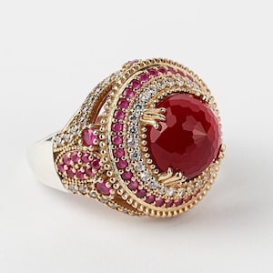 May include: A silver ring with a large red gemstone surrounded by smaller red and white gemstones.