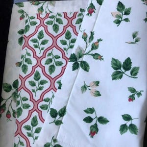 May include: Two fabric swatches with floral patterns. One swatch features a white background with green leaves and pink roses. The other swatch features a white background with a pink and red geometric pattern.