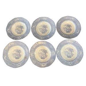 May include: Six blue and white decorative plates. Each plate features a central landscape scene with a tree and building, surrounded by a patterned border. The plates are arranged in a symmetrical pattern.