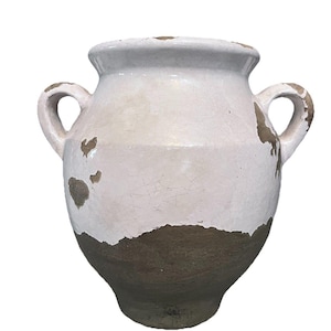 May include: A white and brown ceramic vase with two handles. The vase has a distressed, aged appearance with a white upper section and a brown lower section. The vase is likely for decorative purposes.