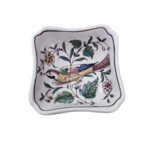 May include: A square, white ceramic dish with a scalloped edge. The dish features a colorful illustration of a bird perched on a flowering branch. The bird has blue, yellow, and purple feathers. The flowers are pink and the leaves are green.