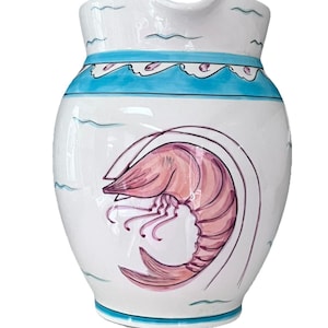 May include: White ceramic jug with a shrimp illustration. The jug has a light blue band with wave-like designs and a matching base. The shrimp is depicted in shades of pink and purple, adding a pop of colour to the design.