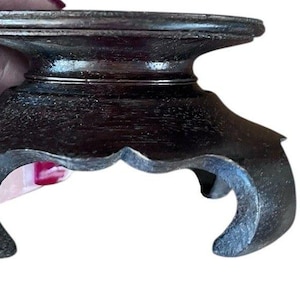 Peut inclure: Un présentoir en bois brun foncé avec un dessus rond et une base décorative festonnée. Le présentoir a un design classique, probablement pour de petits objets. Le grain du bois est visible, ajoutant à son attrait vintage.