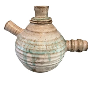 Peut inclure: Un récipient en céramique fait à la main avec un corps bulbeux et deux becs. La poterie présente une base beige clair avec des rainures horizontales et des stries d'émail turquoise pâle. Le récipient a un petit col cylindrique et un couvercle.