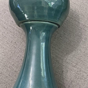 May include: A teal-colored ceramic pedestal planter with a bulbous top and flared base. The planter has a glossy finish and a smooth, curved design. It is suitable for indoor or outdoor use.