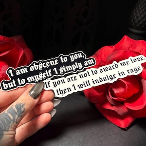 May include: Two stickers with gothic text are held near red roses. One sticker reads "I am obscene to you, but to myself I simply am." The other says "If you are not to award me love, then I will indulge in rage."