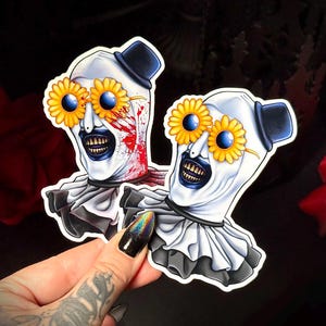 Peut inclure: Deux autocollants représentant un clown effrayant avec du maquillage blanc, un chapeau haut de forme noir et un col à volants. Le clown porte des lunettes en forme de tournesol. Un clown a des éclaboussures de sang sur le visage. Le fond est sombre avec une rose rouge.