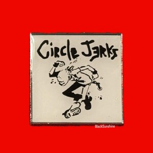 May include: A white enamel pin with a black and white illustration of a person skateboarding. The text "Circle Jerks" is printed in black at the top of the pin.