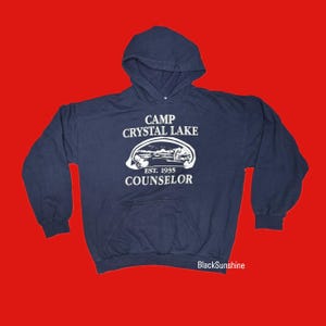 May include: A navy blue hooded sweatshirt with the text "Camp Crystal Lake Est. 1935 Counselor" in white.