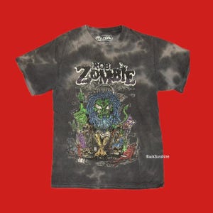 May include: Dark gray tie-dye t-shirt featuring a graphic of a green-faced character with blue hair, surrounded by other cartoonish figures. The text "ROB ZOMBIE" is displayed above the central image. The shirt has a Global brand tag.