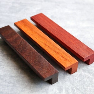 May include: Three wooden cabinet pulls in different shades of brown. The pulls are rectangular with a slight curve at the bottom.