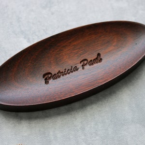 May include: A dark brown oval wooden dish with the name "Patricia Paul" engraved in the center.