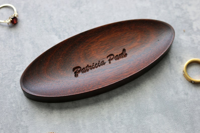 May include: A dark brown oval wooden dish with the name "Patricia Paul" engraved in the center.