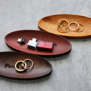 May include: Three oval wooden trays, one with the inscription "Patricia", one with a red and white USB drive and a white USB adapter, and one with gold rings.