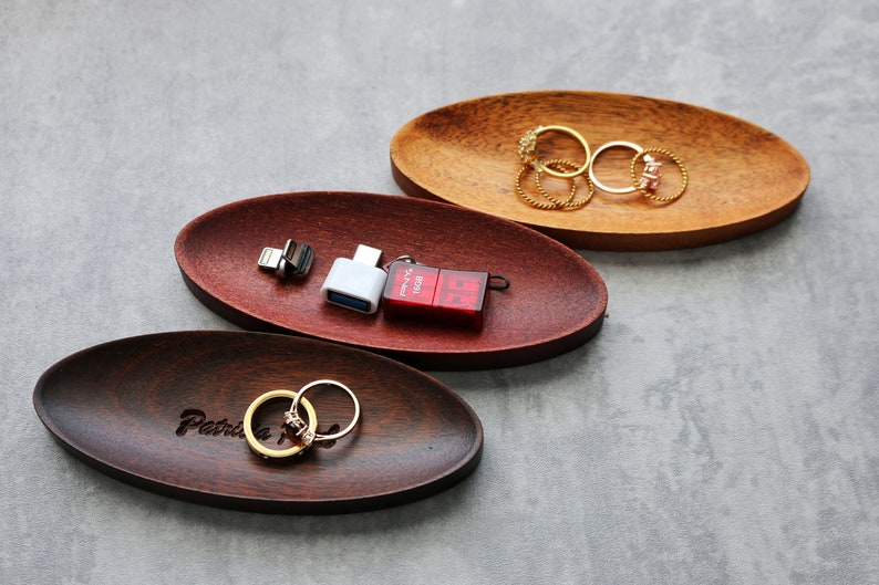 May include: Three oval wooden trays, one with the inscription "Patricia", one with a red and white USB drive and a white USB adapter, and one with gold rings.