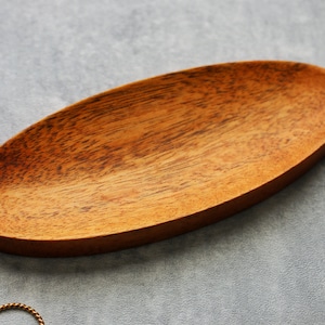 May include: A wooden oval-shaped dish with a natural wood grain finish. The dish is perfect for holding small items like jewelry or keys.