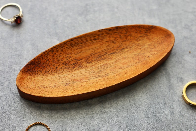 May include: A wooden oval-shaped dish with a natural wood grain finish. The dish is perfect for holding small items like jewelry or keys.