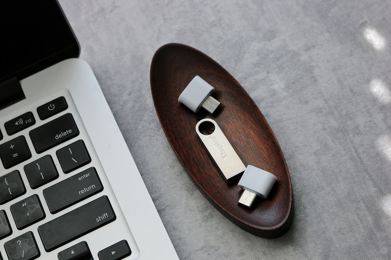 May include: Two silver USB adapters with white plastic casings, one with the text "Kingston" printed on it, are sitting in a wooden oval dish.