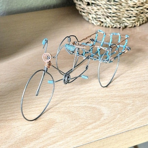 May include: A wire sculpture of a bicycle rickshaw with a blue and copper wire frame. The sculpture is made of thin wire and is very detailed.