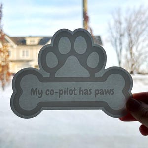 May include: White car sticker shaped like a bone with a paw print on top. The bone has the text "My co-pilot has paws" on it.