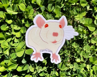 May include: White rat sticker with red eyes and pink ears. The sticker is on a green clover background. The sticker has the text "Camille Caron" on the bottom.