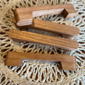 May include: Three wooden drawer pulls with a simple, rectangular design. The pulls are made of light brown wood and have a smooth finish.