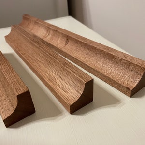 May include: Three wooden trim pieces with rounded edges. The trim pieces are stained a dark brown colour.