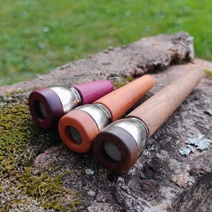 May include: Three tapered wooden smoking pipes with silver-toned metal bowls and mesh screens. The pipes feature distinct wood finishes in purple, light orange, and dark brown, each with a cylindrical stem and a circular opening at the end.