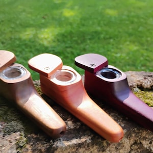 May include: Three wooden smoking pipes arranged side by side. Each pipe features a smooth, tapered body, a circular glass bowl insert, and a small, swiveling wooden lid secured with a single screw. The pipes are finished in dark brown, light brown, and deep purple wood tones.