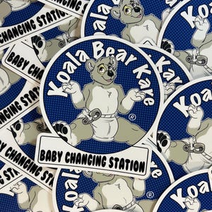 Puede incluir: Una colección de pegatinas con un oso koala de dibujos animados con pañales. El koala está rodeado por las palabras "Koala Bear Kare" en un círculo azul con un borde blanco. Las pegatinas rectangulares dicen "Baby Changing Station."
