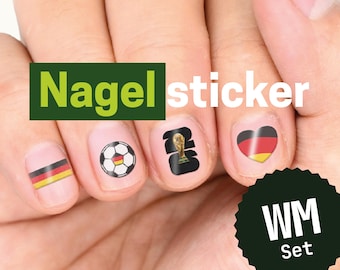 Op de afbeelding: Een set nagelstickers met ontwerpen in Duits thema, waaronder een horizontale driekleurige vlag, een voetbal met vlagpatroon, een gouden trofee-icoon en een hart met de kleuren van de Duitse vlag. De tekst Nagel sticker en WM Set zijn zichtbaar.