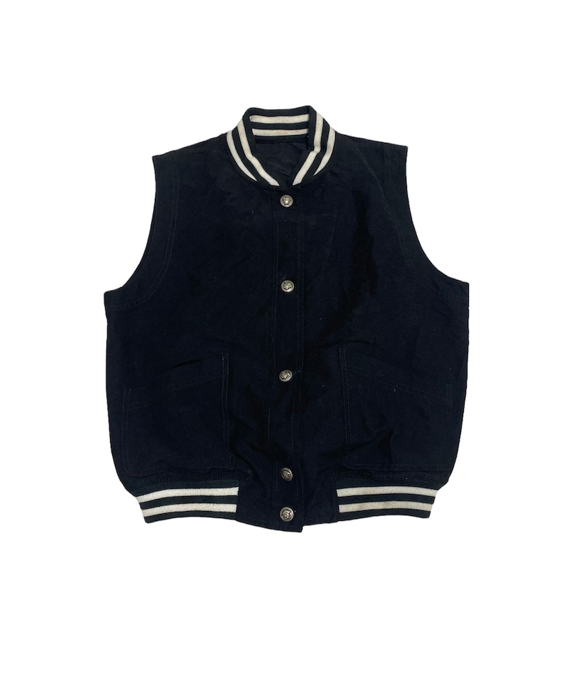 May include: A black sleeveless button-up vest with white striped trim around the collar and bottom hem. The vest has two pockets and is made of a soft, textured fabric.