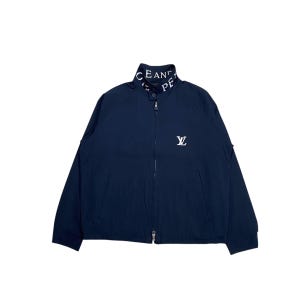 May include: Navy blue zip-up jacket with a stand-up collar. The collar features the text "CEAN PE" in white. A white "LV" logo is on the chest. The jacket has two front pockets and a full zipper closure.